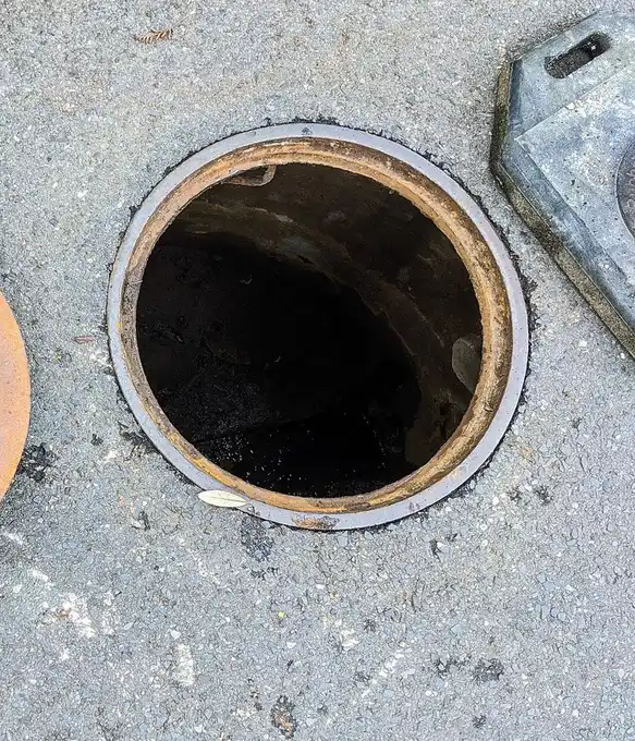 Regard d'égout rond ouvert dans une chaussée en enrobé, son couvercle en fonte posé à côté