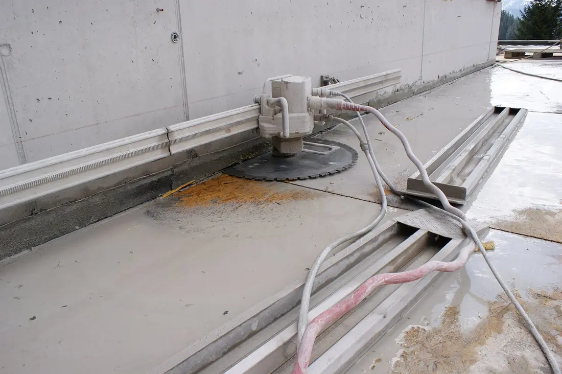 Scie murale à disque diamant sur rail fixé contre un mur en béton, dalle humide et flexibles au sol, sans opérateur