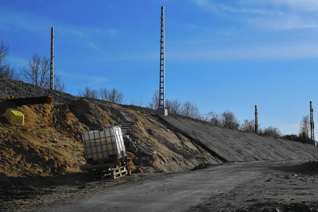 Talus de terre sableuse en cours d'aménagement avec partie lissée, cuve IBC sur palettes au pied
