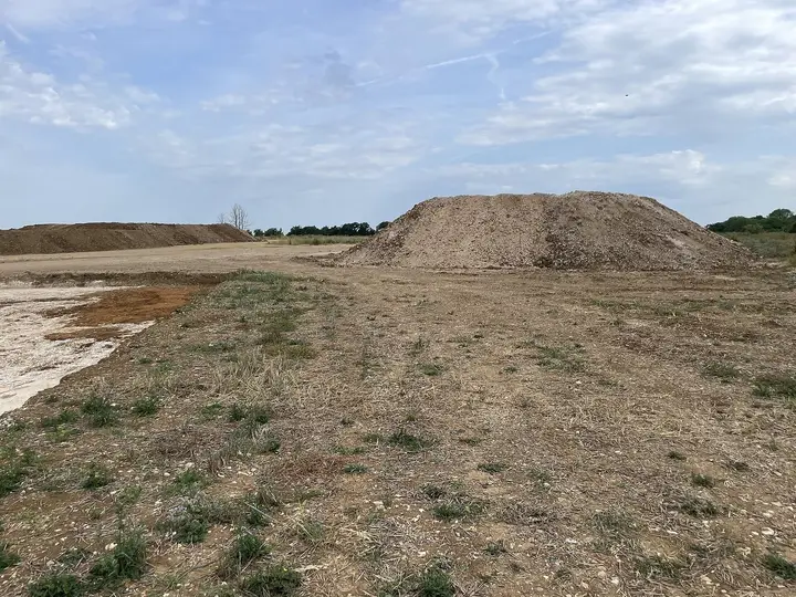 Gros tas de terre et de cailloux sur un terrain décapé, grand ciel nuageux